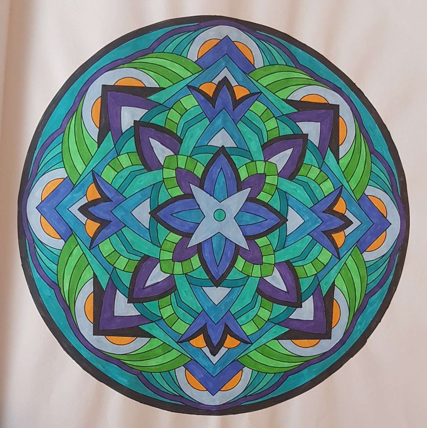A mandala starting with blue 4 pointed star shapes in the middle, with purple-pointed leaf shapes around that, and some semi circlular shapes in green